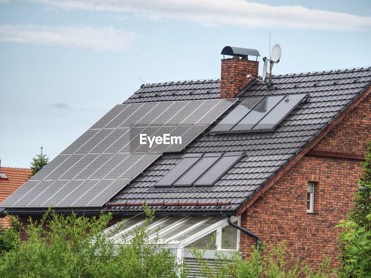 Large solar panels on roof of house. horizontal orientation, blue sky, gray panels on brown roof.