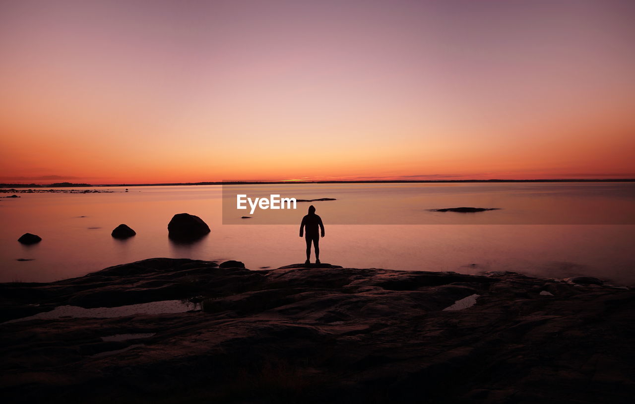 Silhouette man standing on rock by sea against sky during sunset