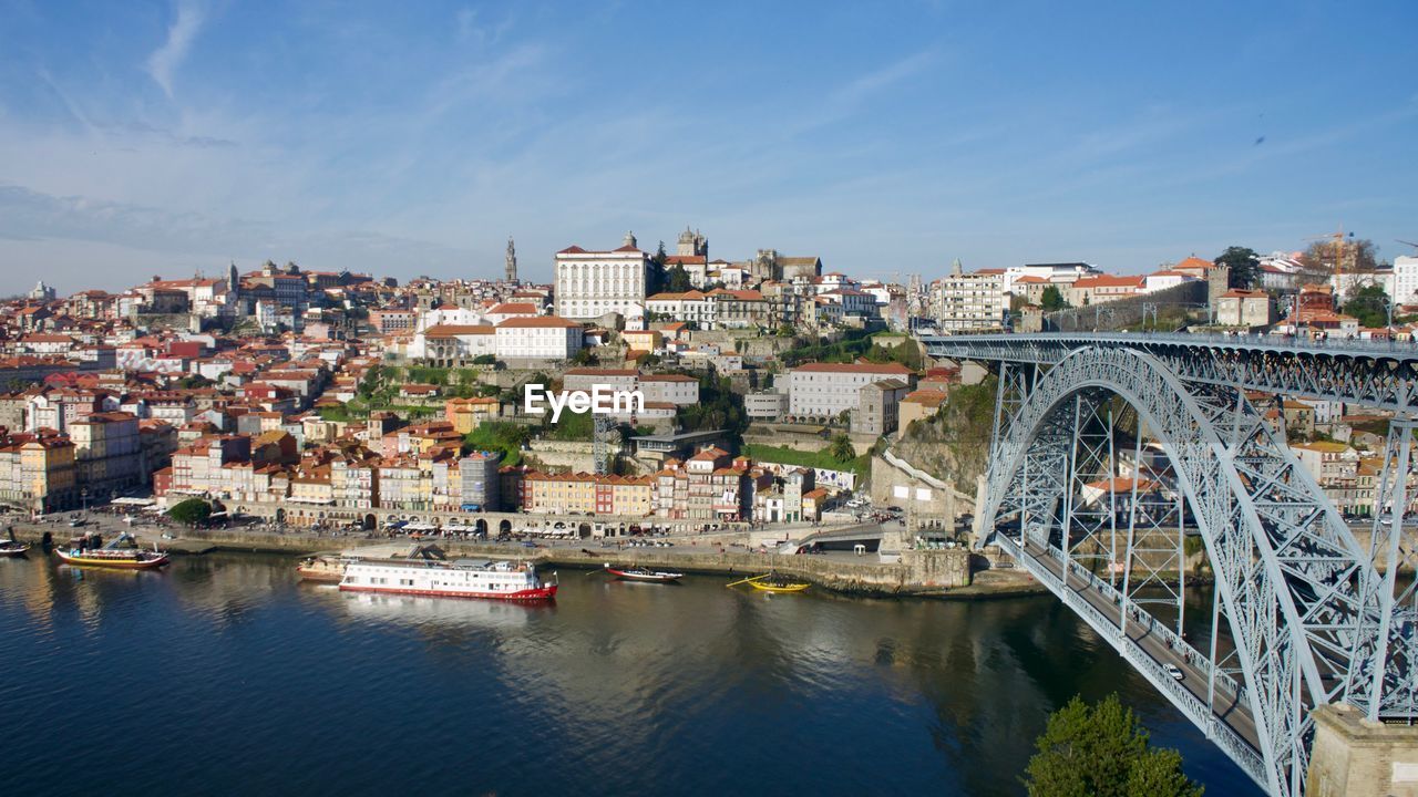 Bridge over river by buildings in city against sky