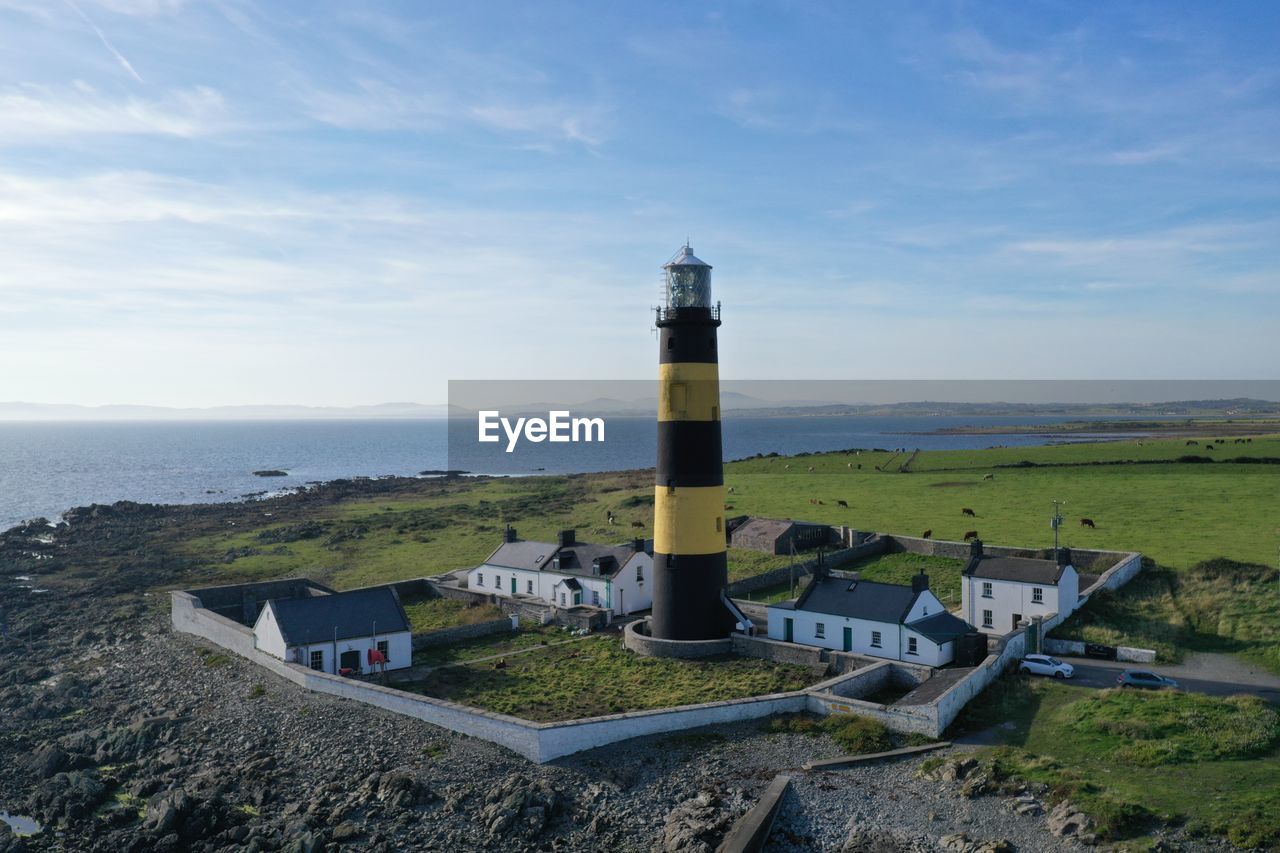 Lighthouse amidst sea and buildings against sky