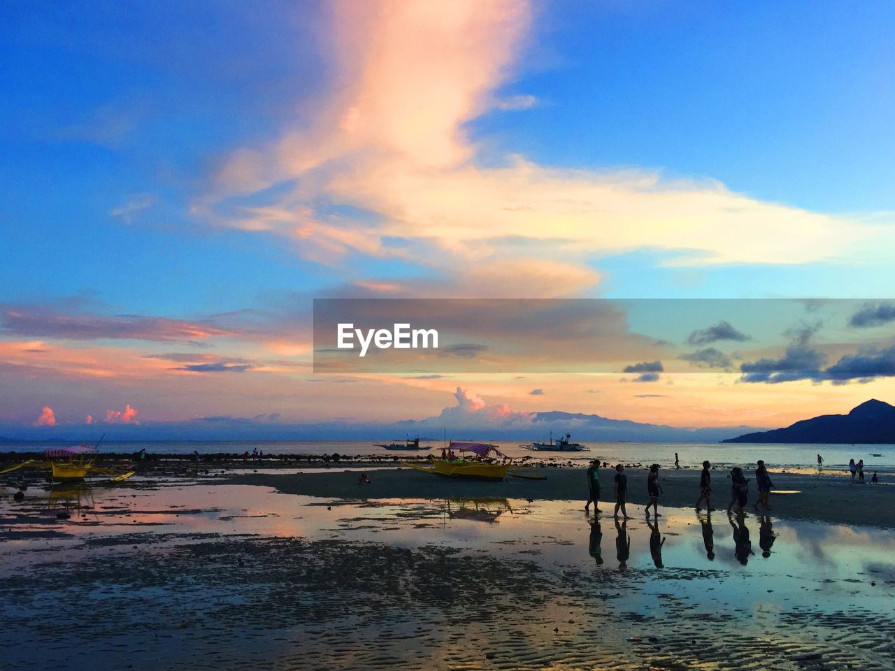People on wet shore at beach against sky