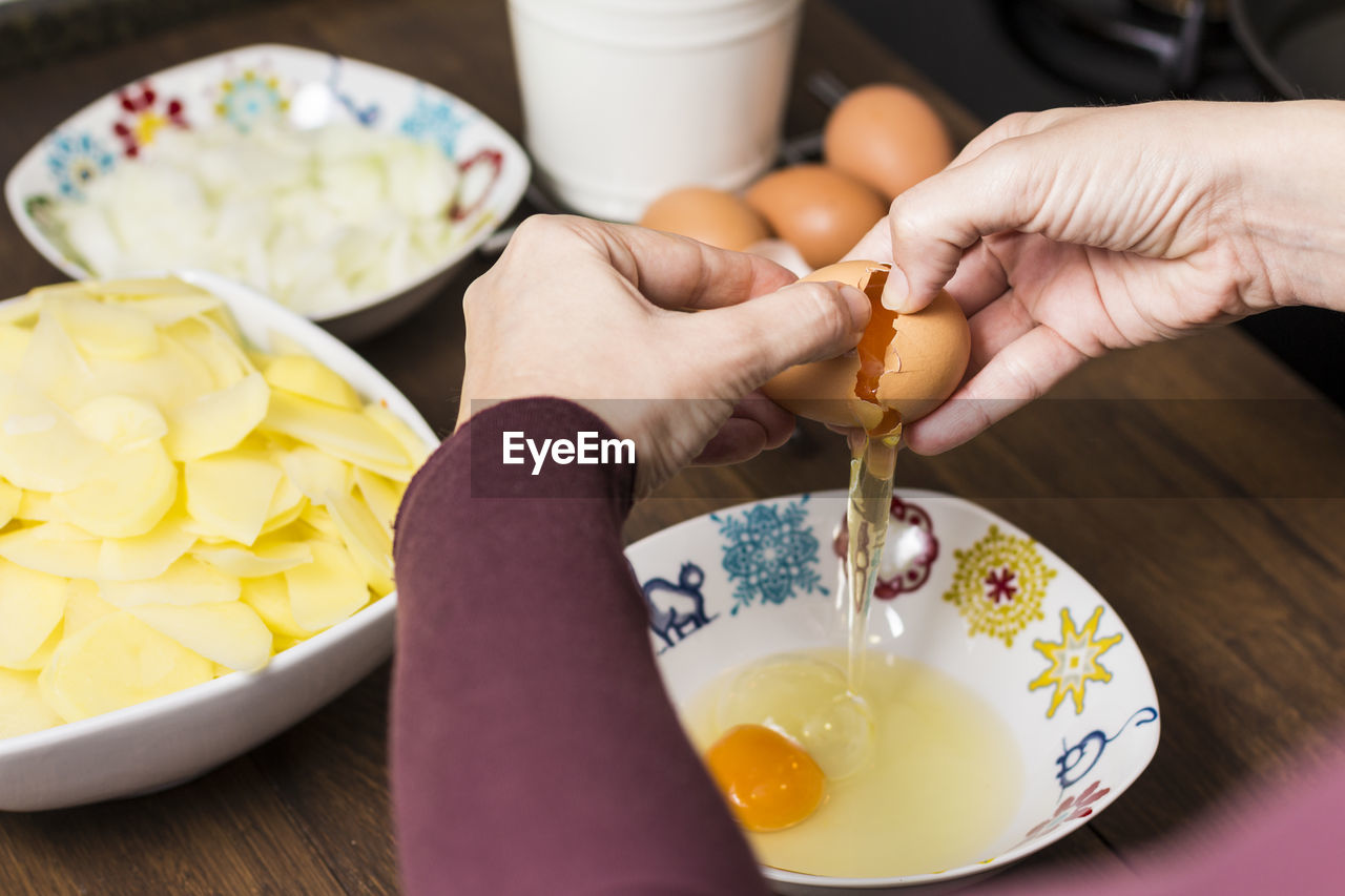 Cropped hands of woman breaking eggs in bowl on table