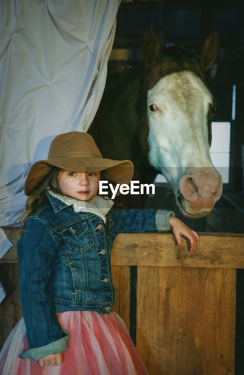 Girl in hat standing by horse