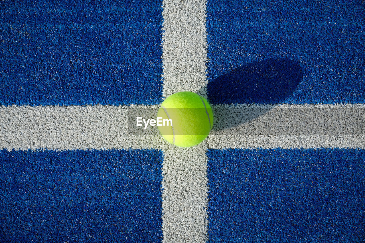 Yellow tennis ball in the court on blue grass - paddle tennis ball on the court on blue turf