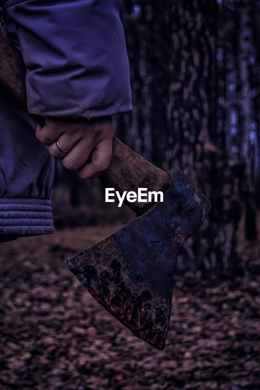 Cropped image of woman holding axe in forest