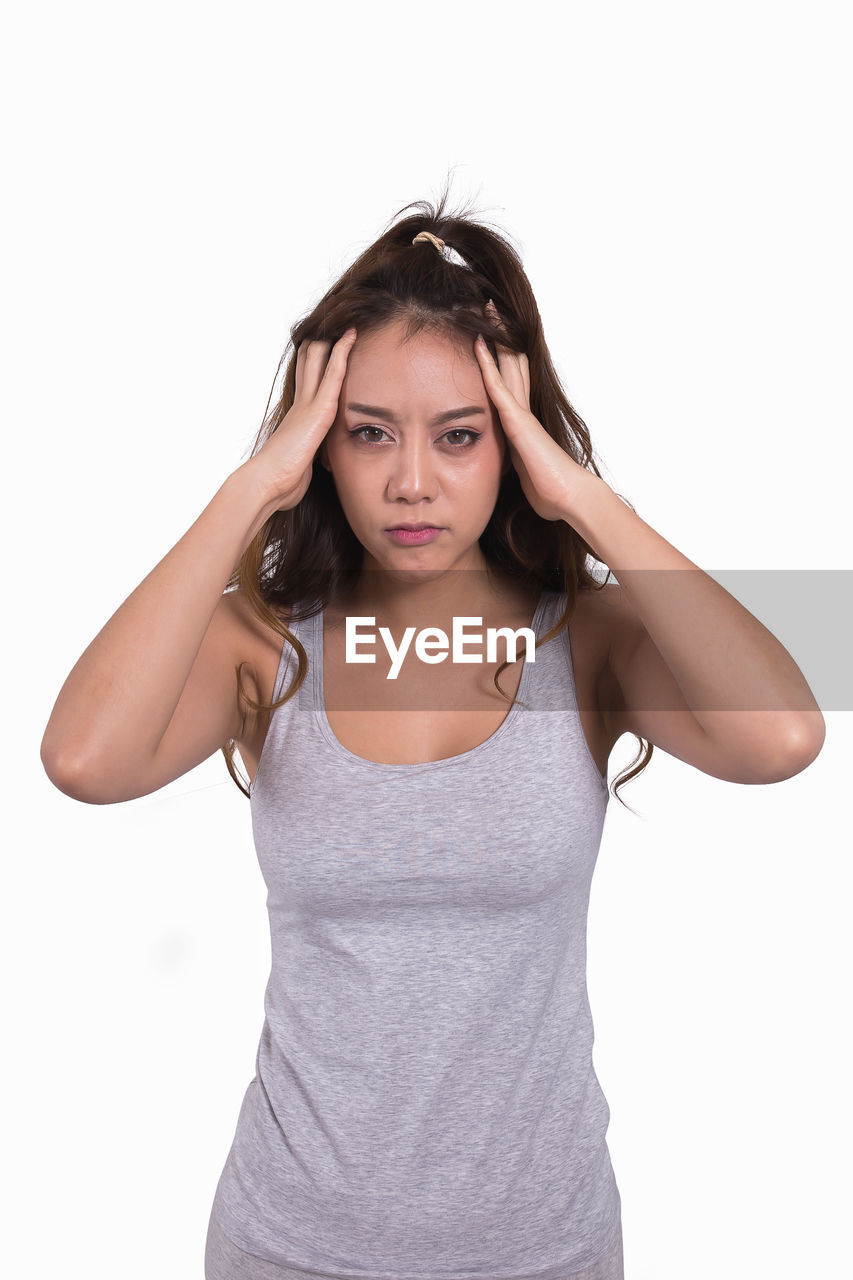 Portrait of young woman with hand in hair standing against white background