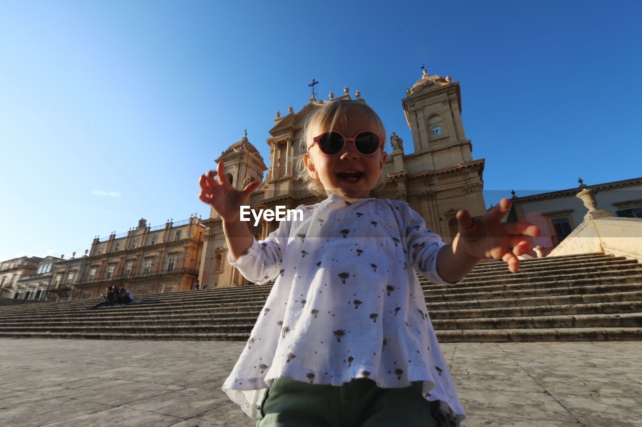 Low angle view of cute baby girl wearing sunglasses while standing against church