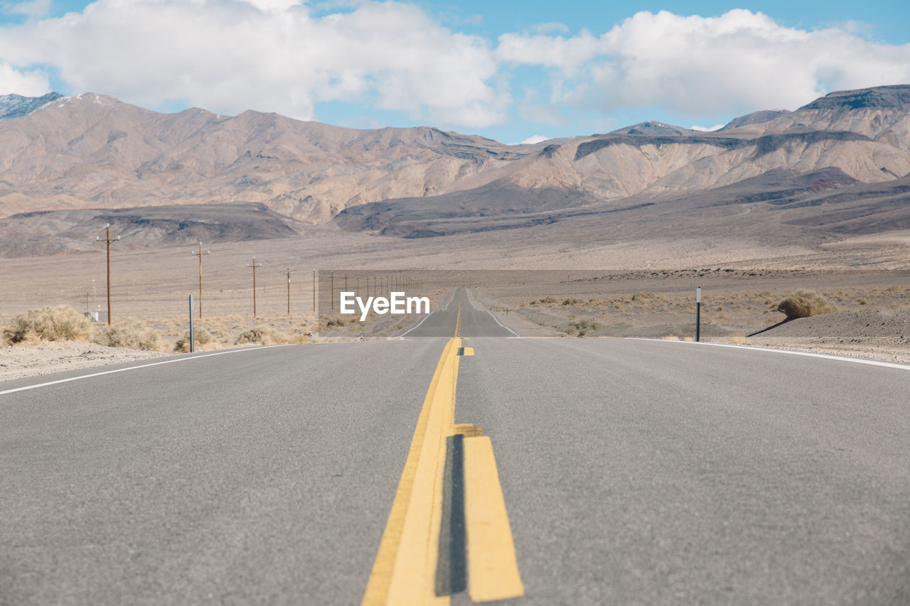 Empty road by mountains against sky