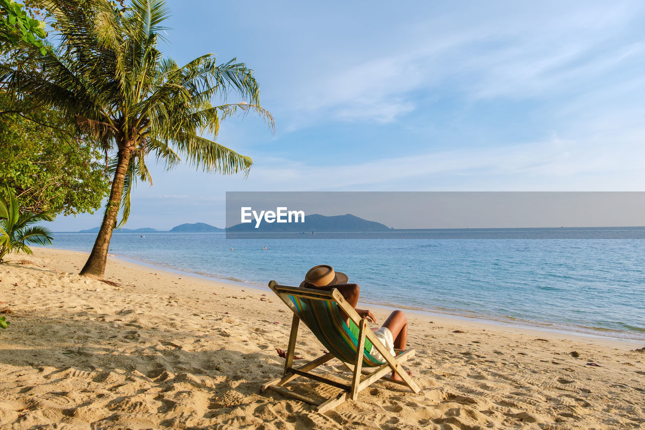 rear view of woman sitting at beach against sky