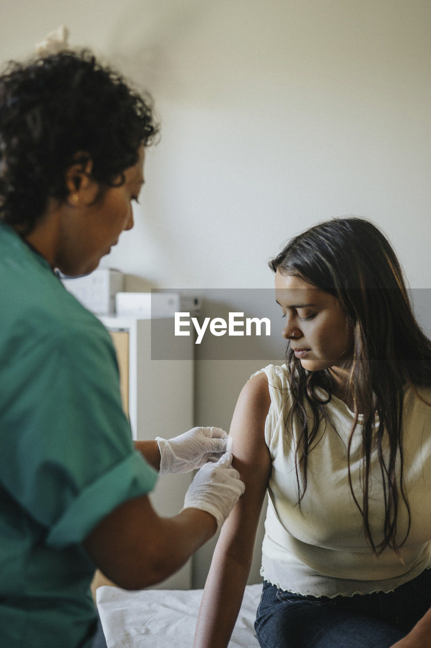 Mature doctor applying bandage on hand of young woman during vaccination in clinic