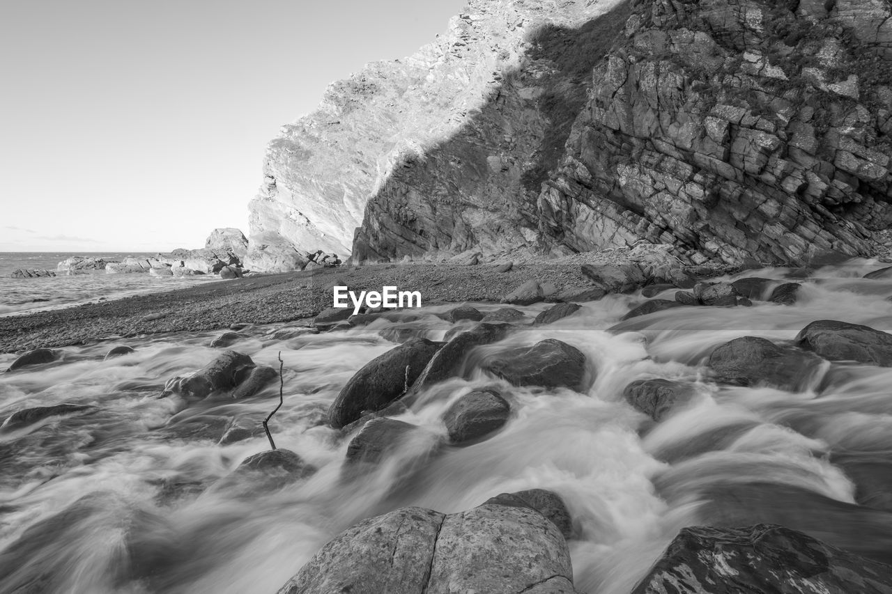 Black and white photo of the river heddon flowing onto the beach at heddons mouth in exmoor