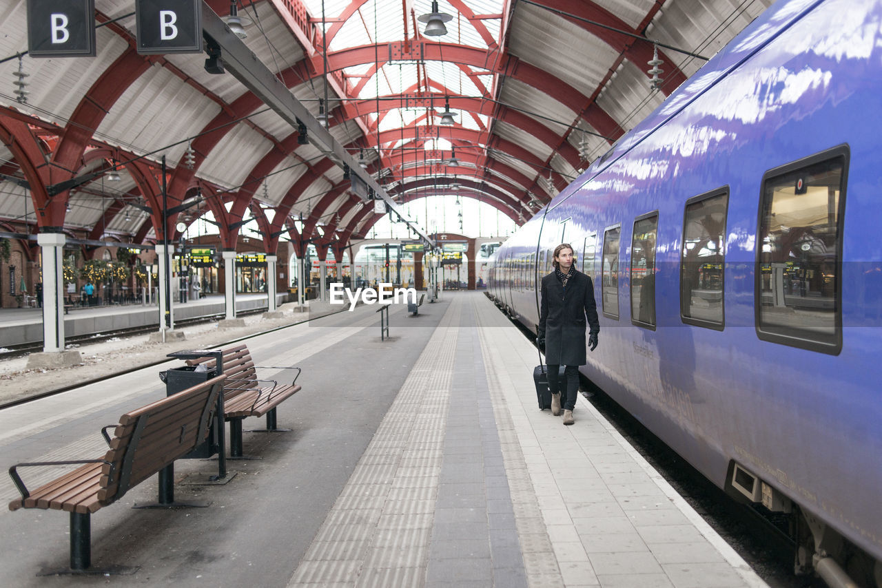 Man with suitcase walking along train at train station