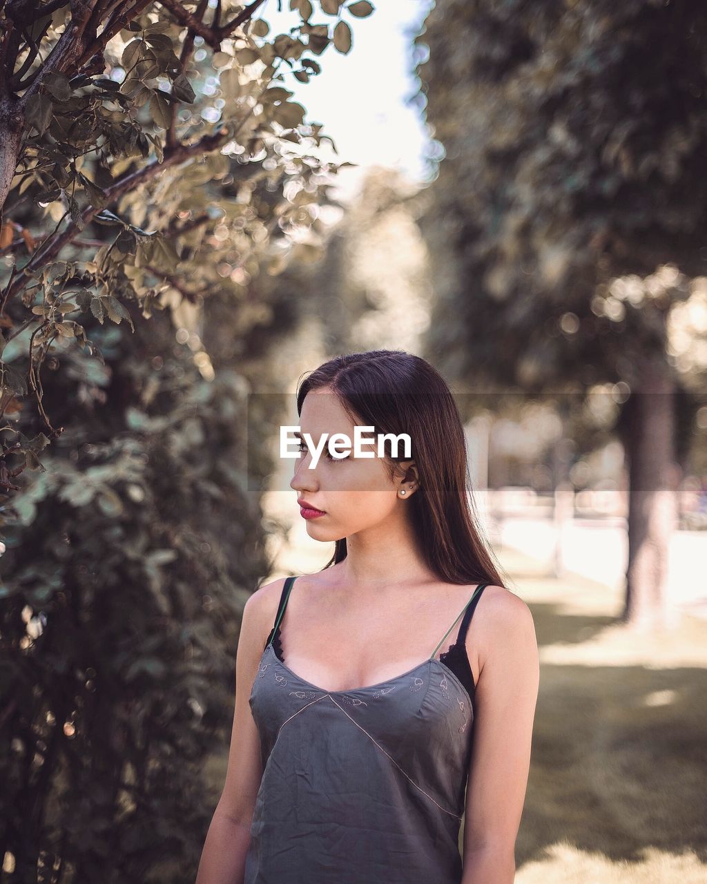 PORTRAIT OF YOUNG WOMAN STANDING AGAINST TREE