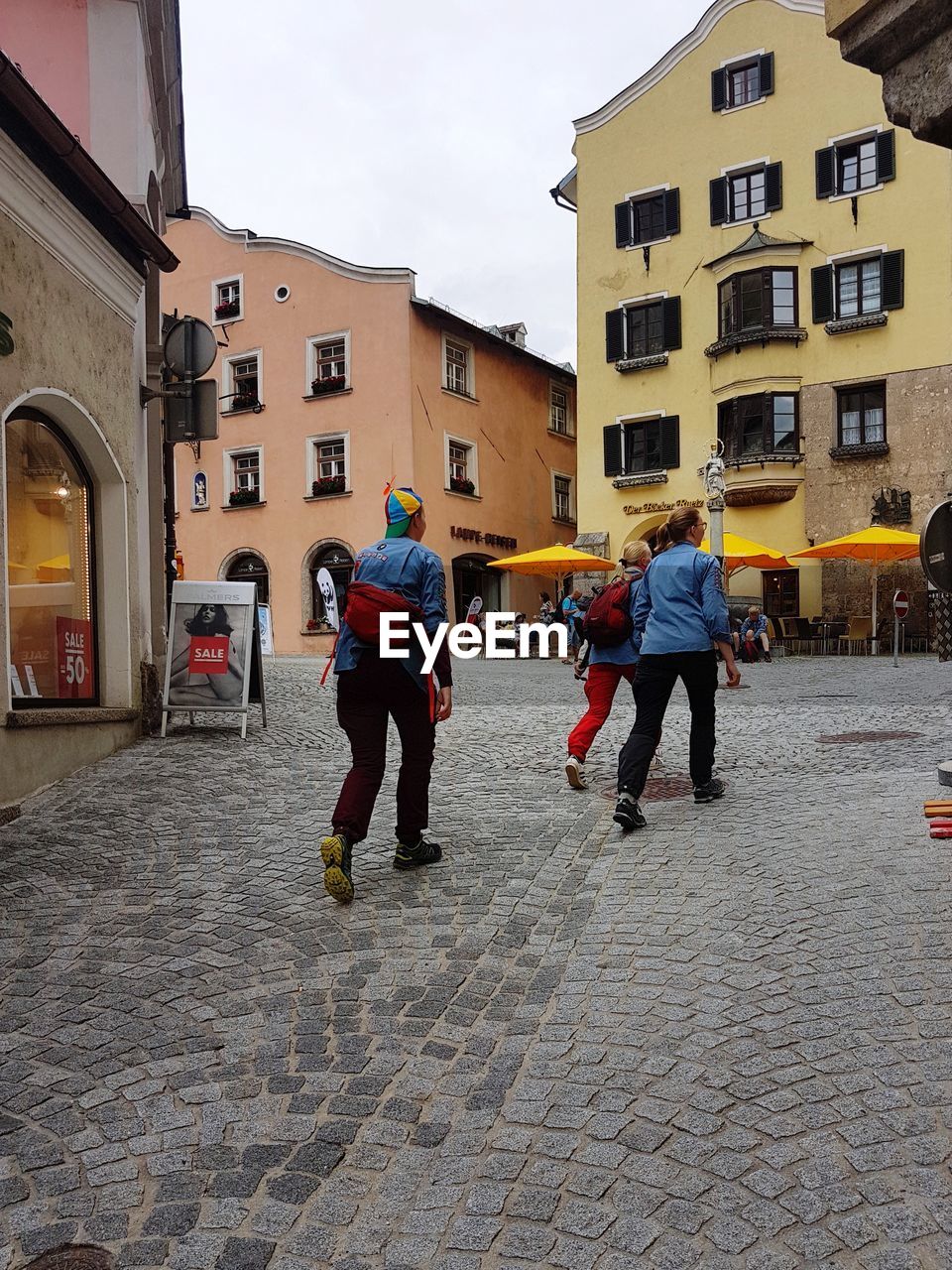 REAR VIEW OF PEOPLE WALKING ON STREET AMIDST BUILDINGS IN CITY