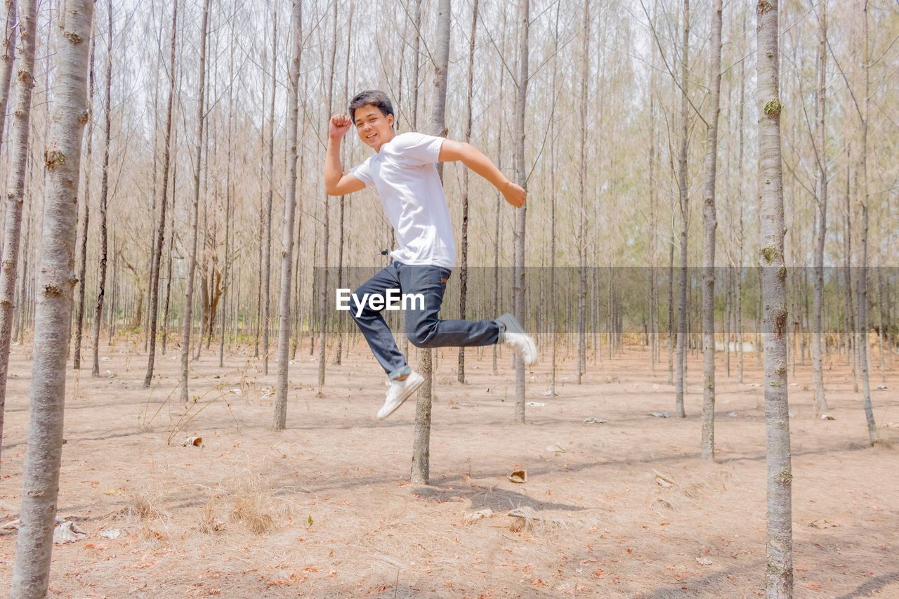Full length portrait of young man jumping at forest