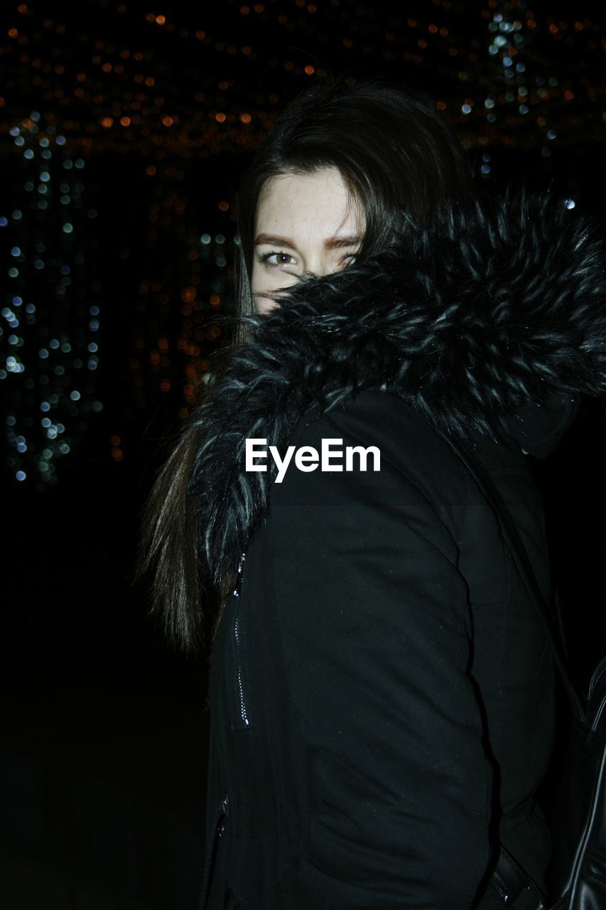 PORTRAIT OF WOMAN STANDING AT NIGHT DURING WINTER AT DUSK