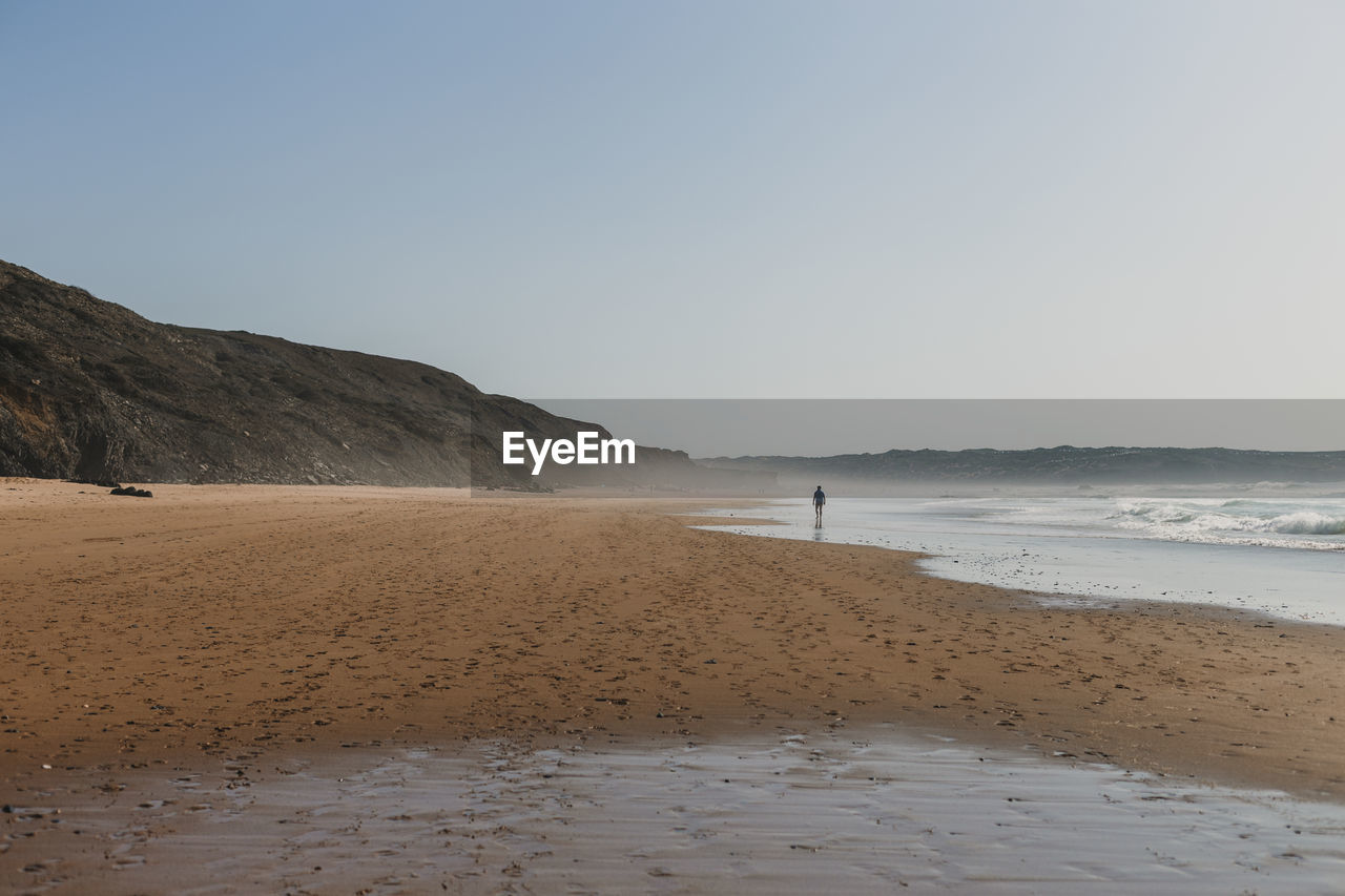 Distant view of man standing at beach against clear sky