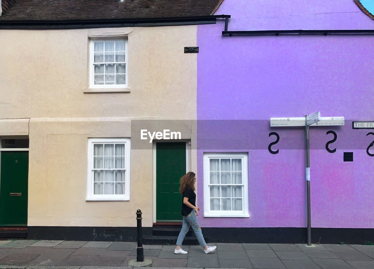 Side view of woman walking on sidewalk against building