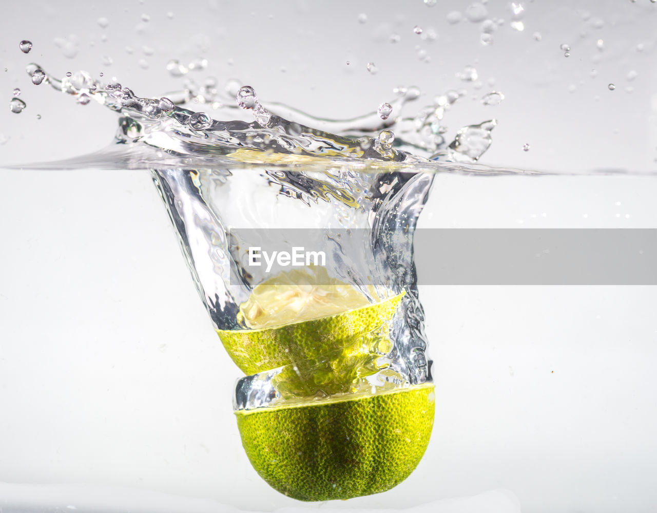 Close-up of limes drop into water splashing in glass against white background