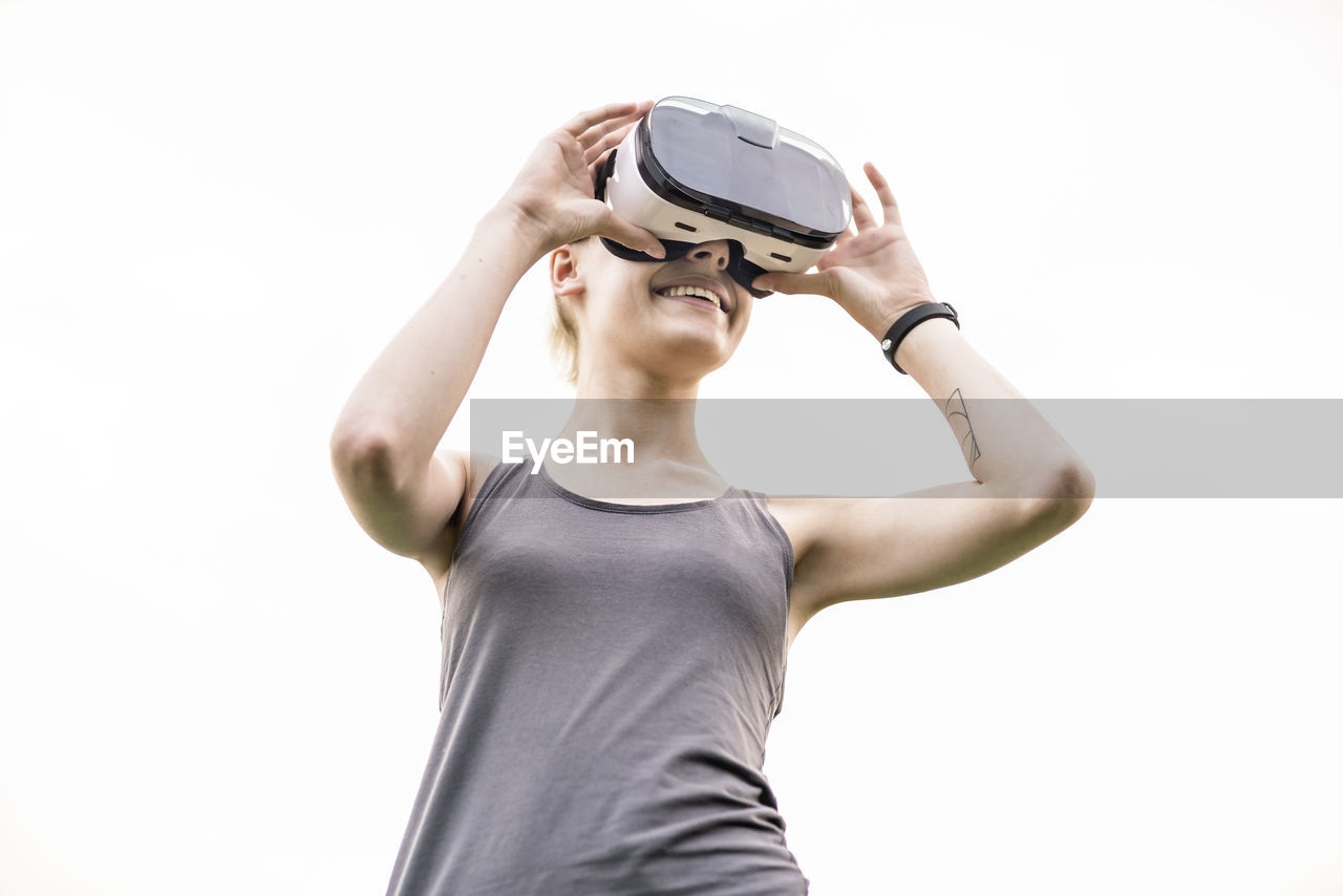 Smiling young woman using virtual reality glasses outdoors