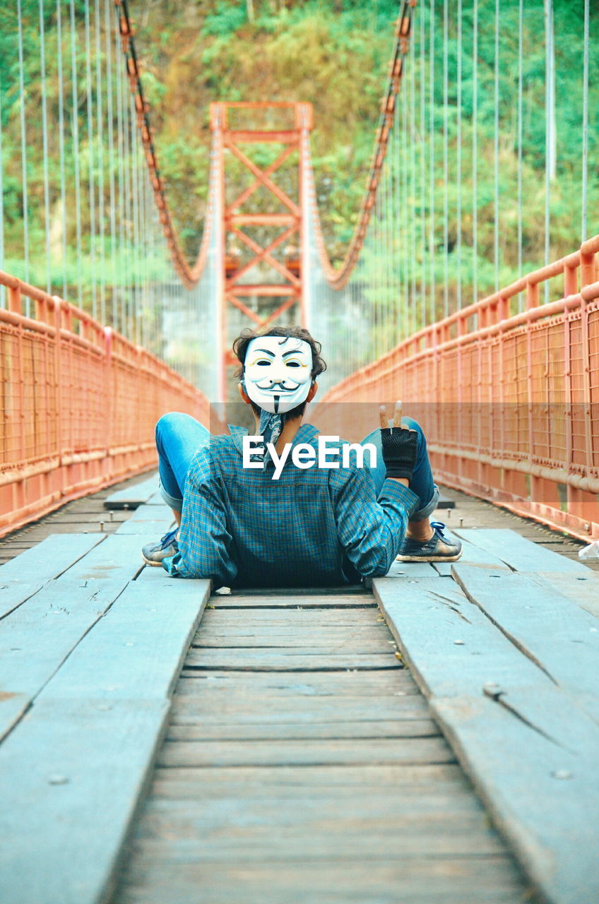 Man wearing mask while lying on footbridge