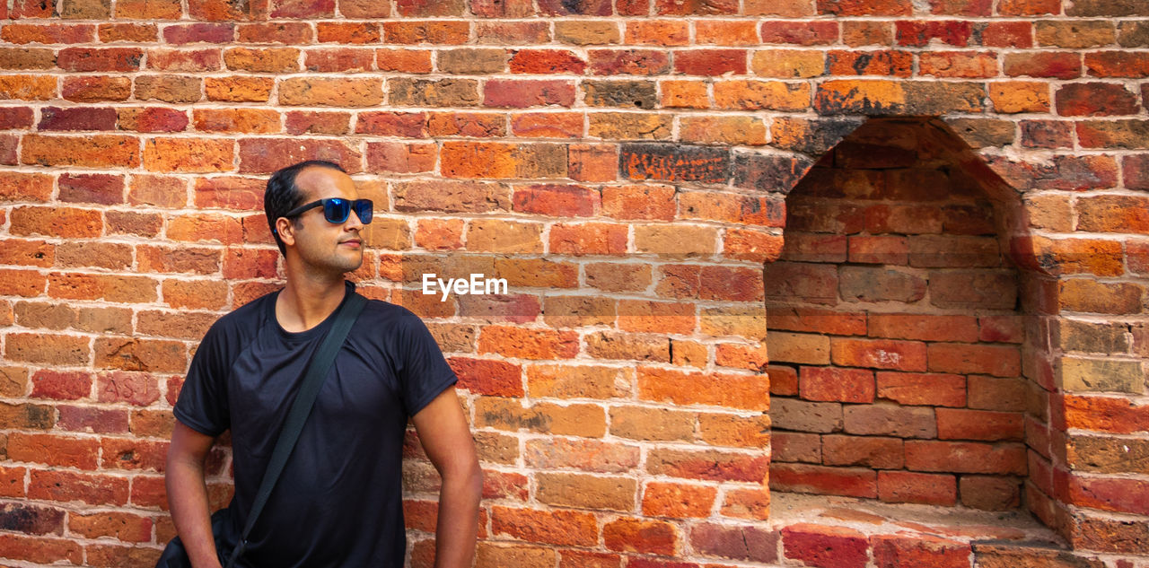 Full length of man standing against brick wall