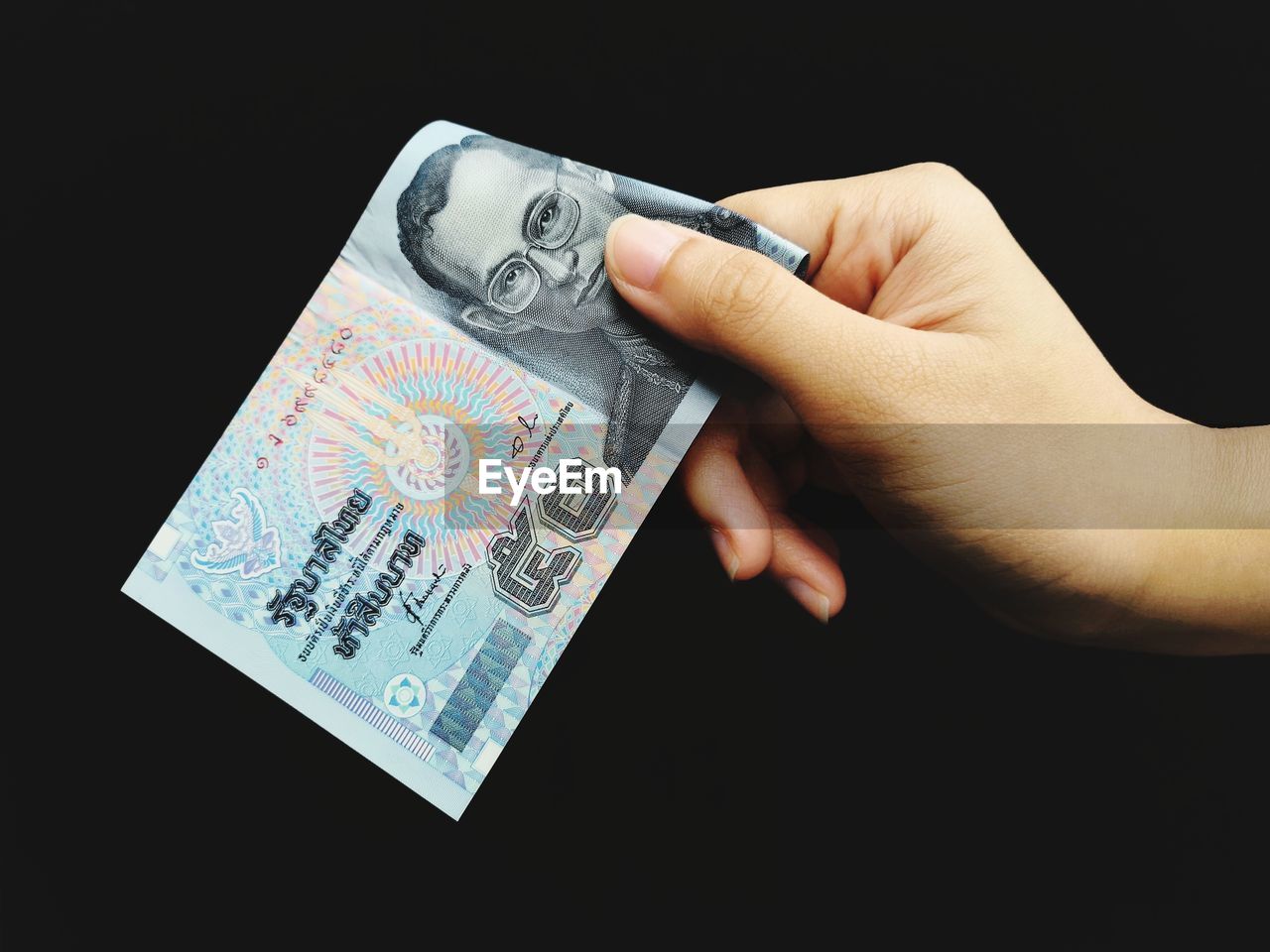 Close-up of hand holding paper currency against black background