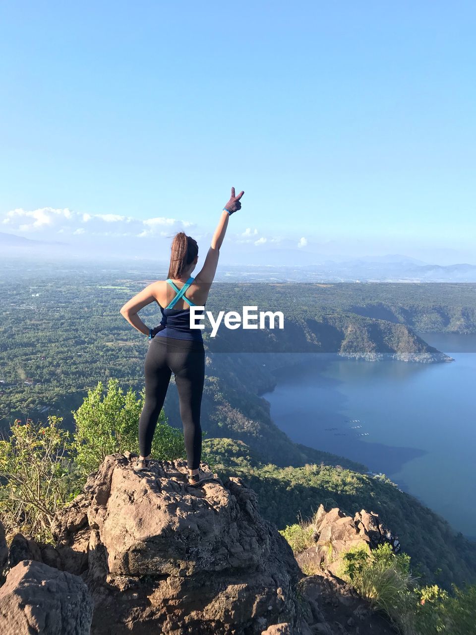 Rear view of woman with hand raised standing on mountain against sky