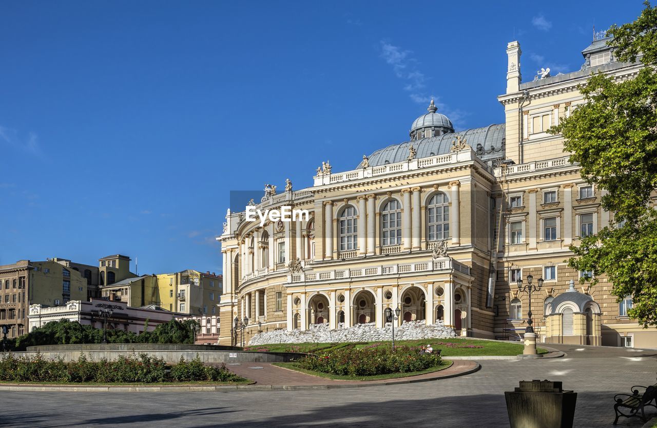 architecture, building exterior, built structure, sky, city, landmark, travel destinations, nature, town square, blue, history, travel, the past, building, palace, clear sky, sunny, town, estate, plaza, day, cityscape, street, no people, tourism, plant, outdoors, downtown, neighbourhood, château, sunlight, facade, tree, government