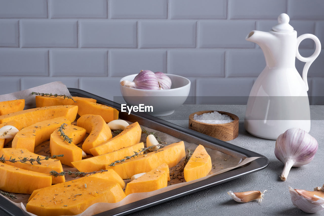 Pieces of ripe pumpkin prepared for baking on a baking sheet with olive oil, garlic and dry thyme 