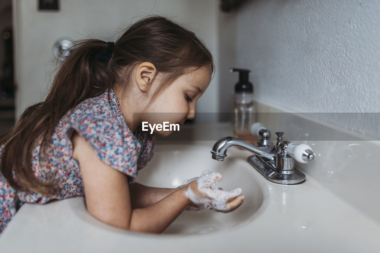 Side view of young girl washing hands in sink with soap