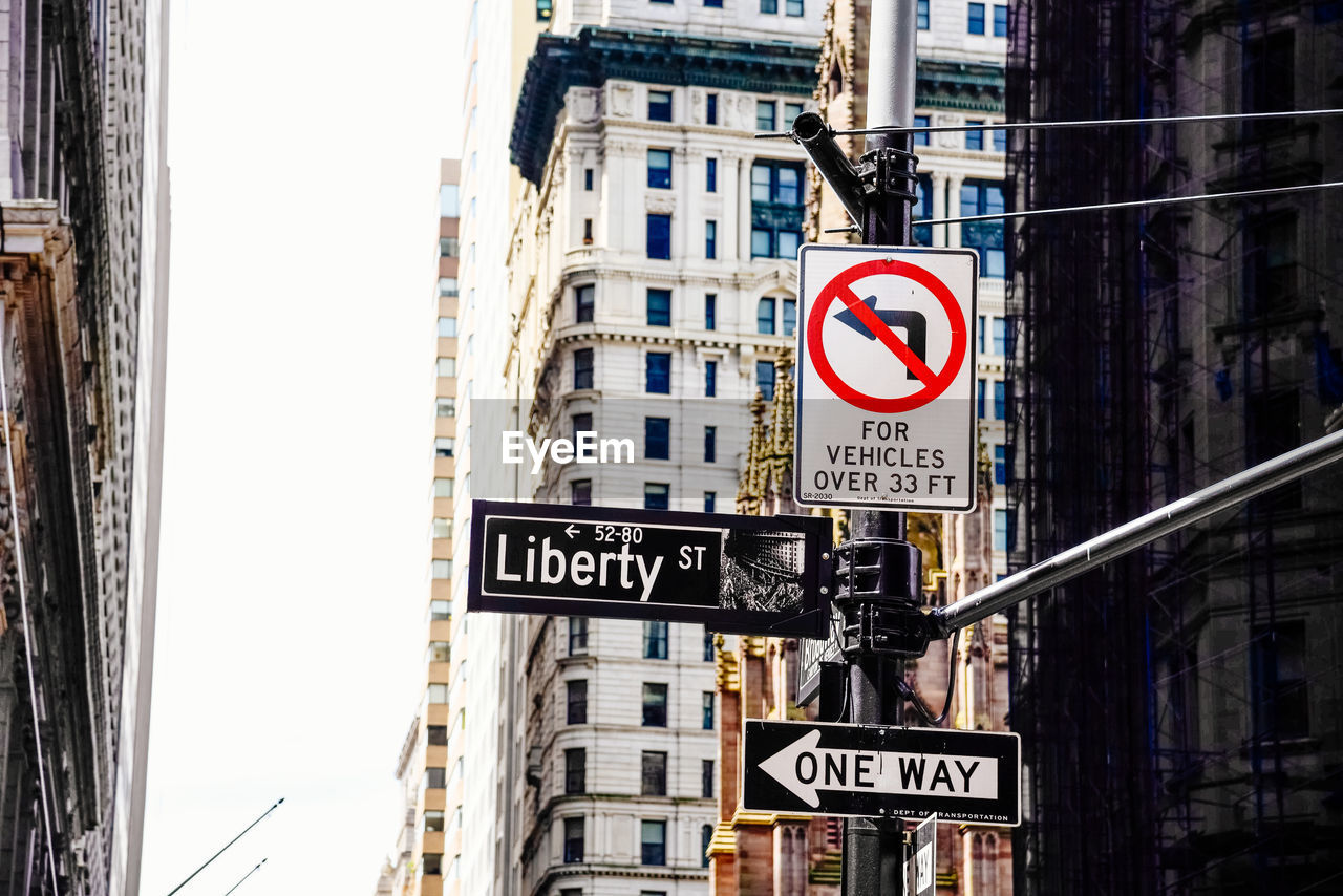 Road sign amidst buildings in city against clear sky