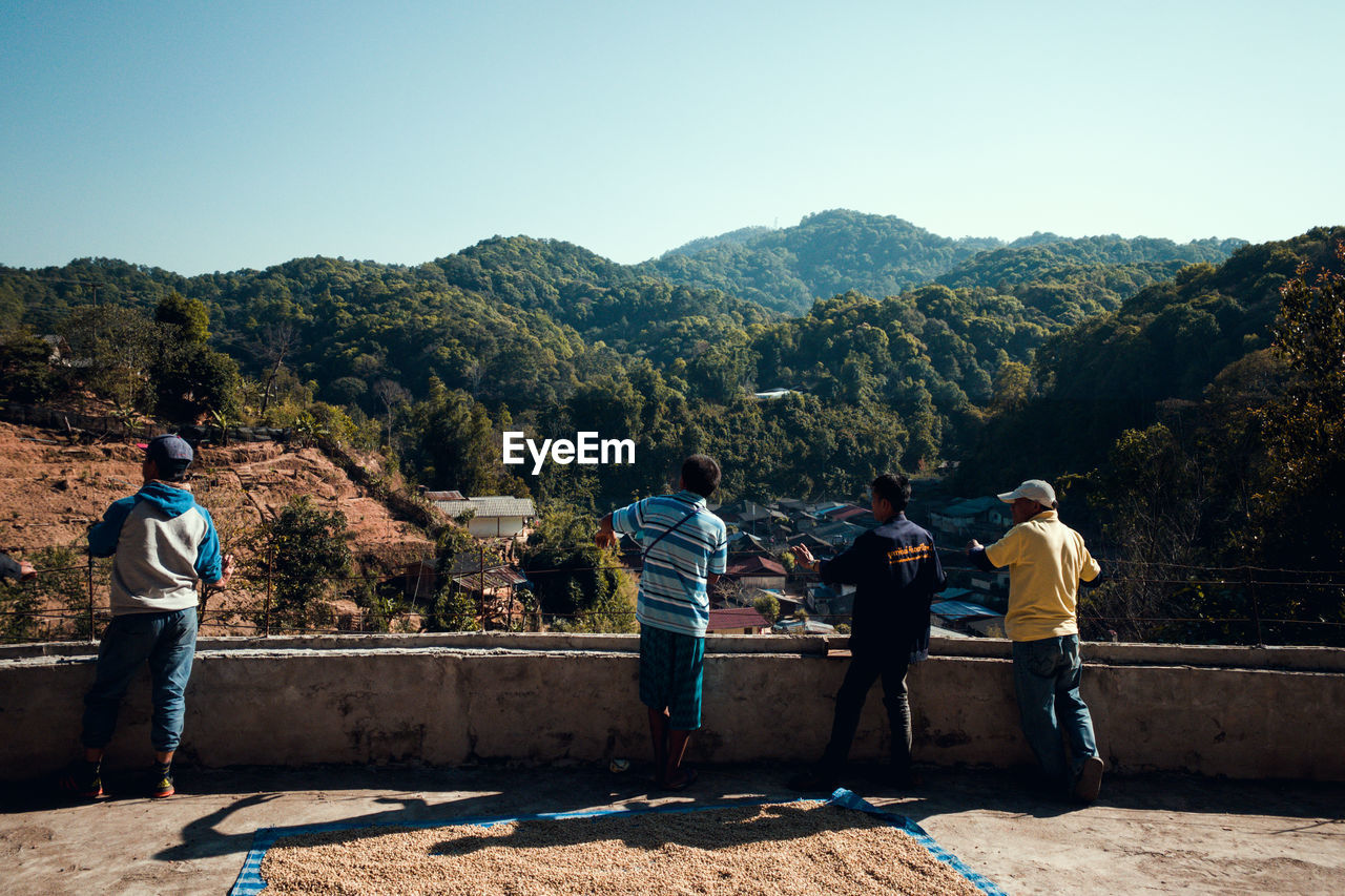 REAR VIEW OF PEOPLE LOOKING AT MOUNTAIN AGAINST SKY