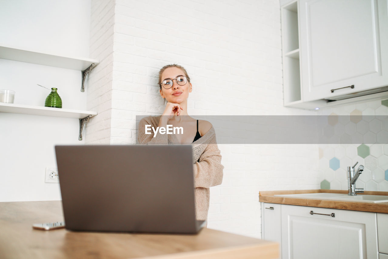 PORTRAIT OF WOMAN USING PHONE WHILE SITTING ON TABLE