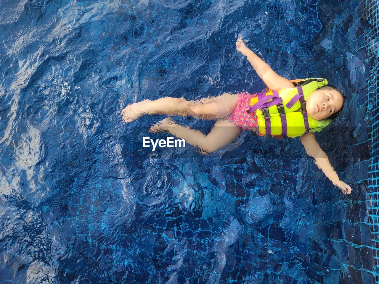 A cute asian girl wearing a pink swimsuit and a green life jacket is playing in the swimming pool.