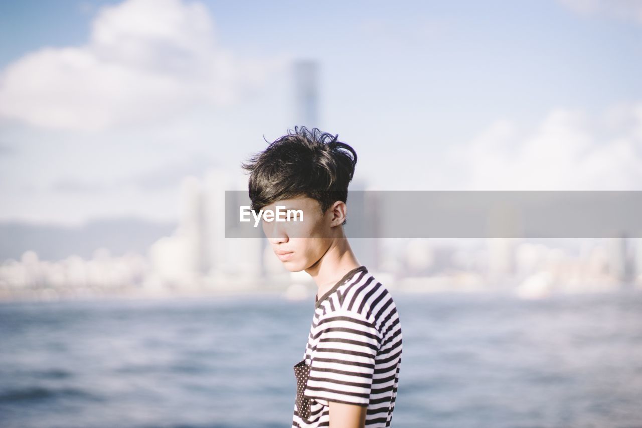 Young man standing by river against sky