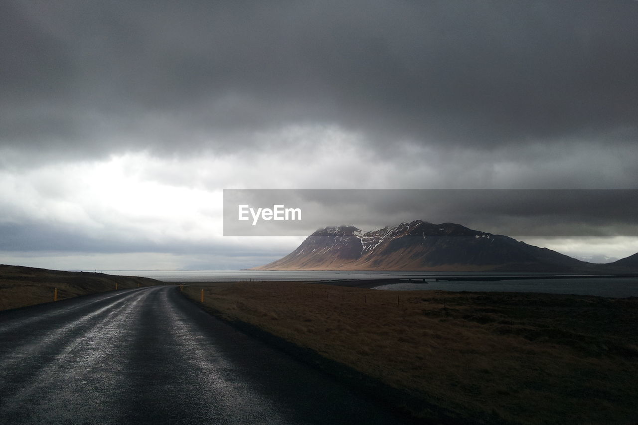 Scenic view of road by beach against storm clouds