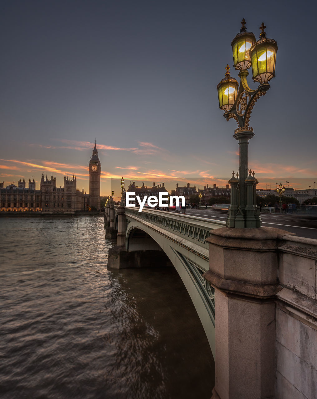 Westminster bridge over thames river by big ben and houses of parliament against sky during sunset