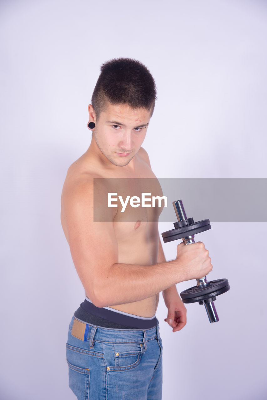 Shirtless man lifting dumbbells against purple background