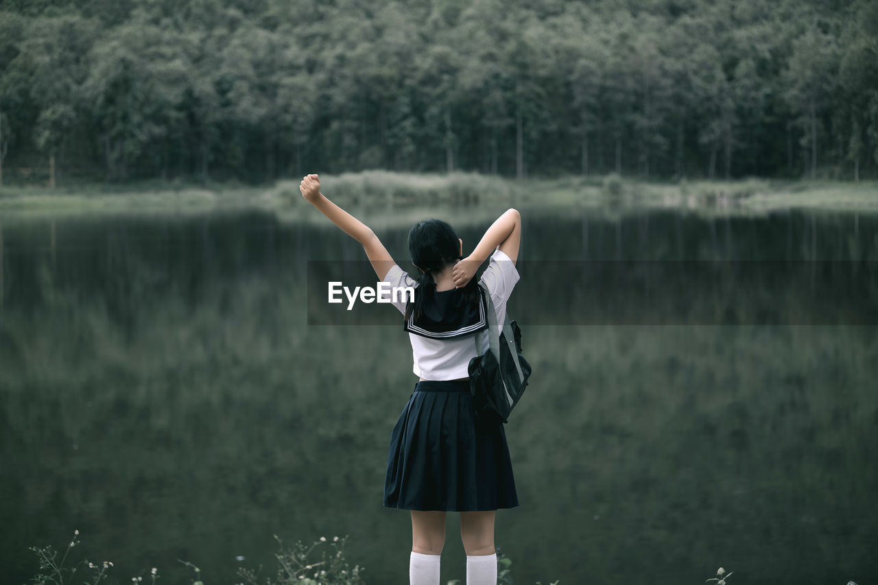 Rear view of woman wearing school uniform while standing against lake