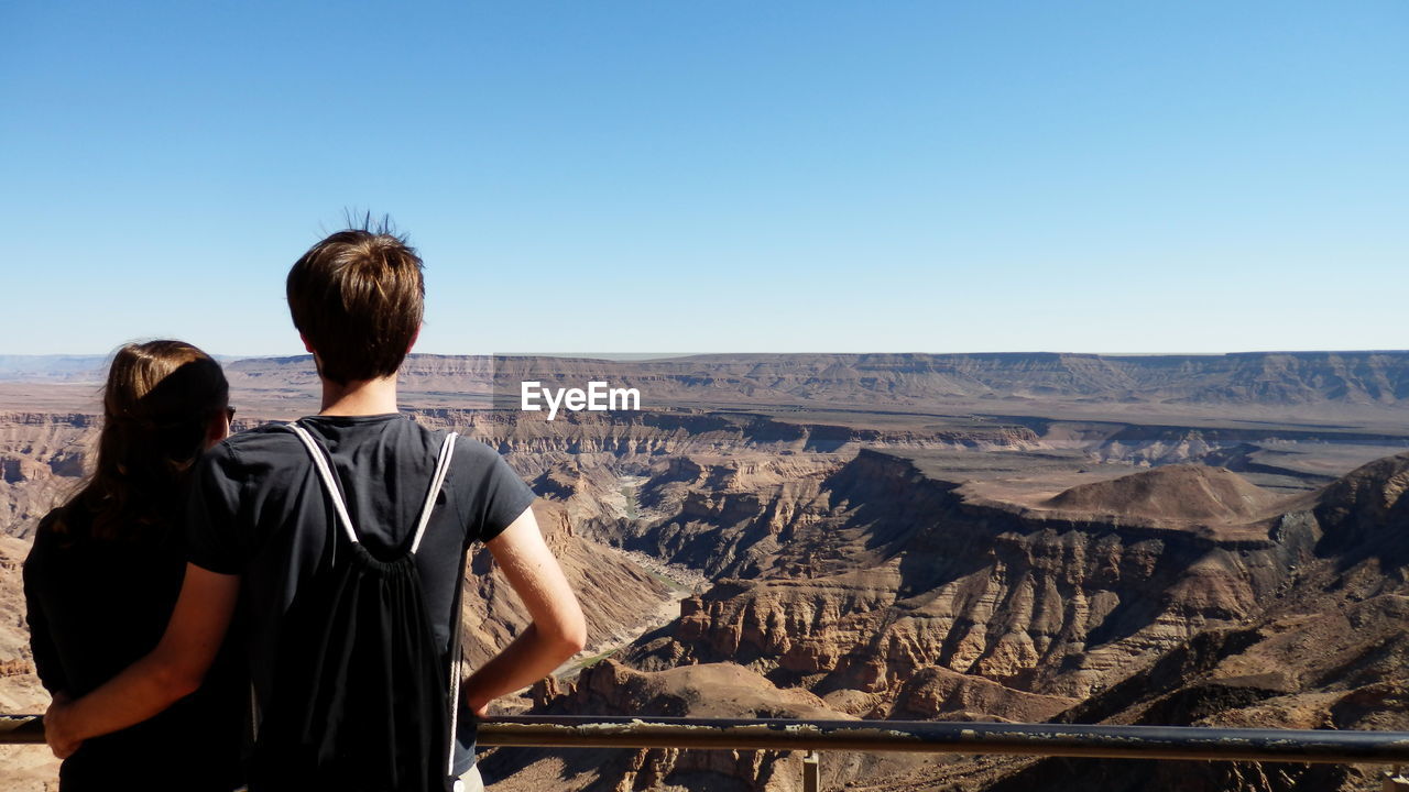 Rear view of people looking at valley against clear sky