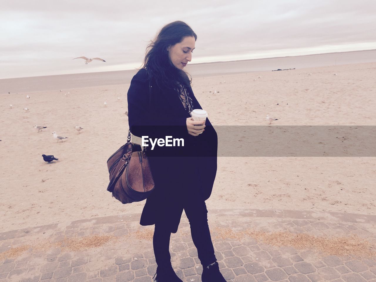 Beautiful young woman with coffee cup standing at beach