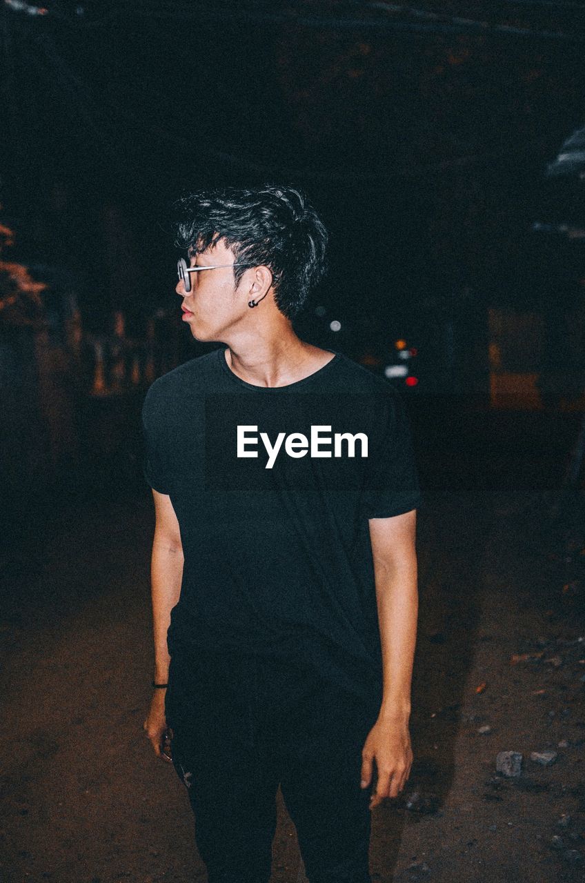 Young man looking away while standing on street at night