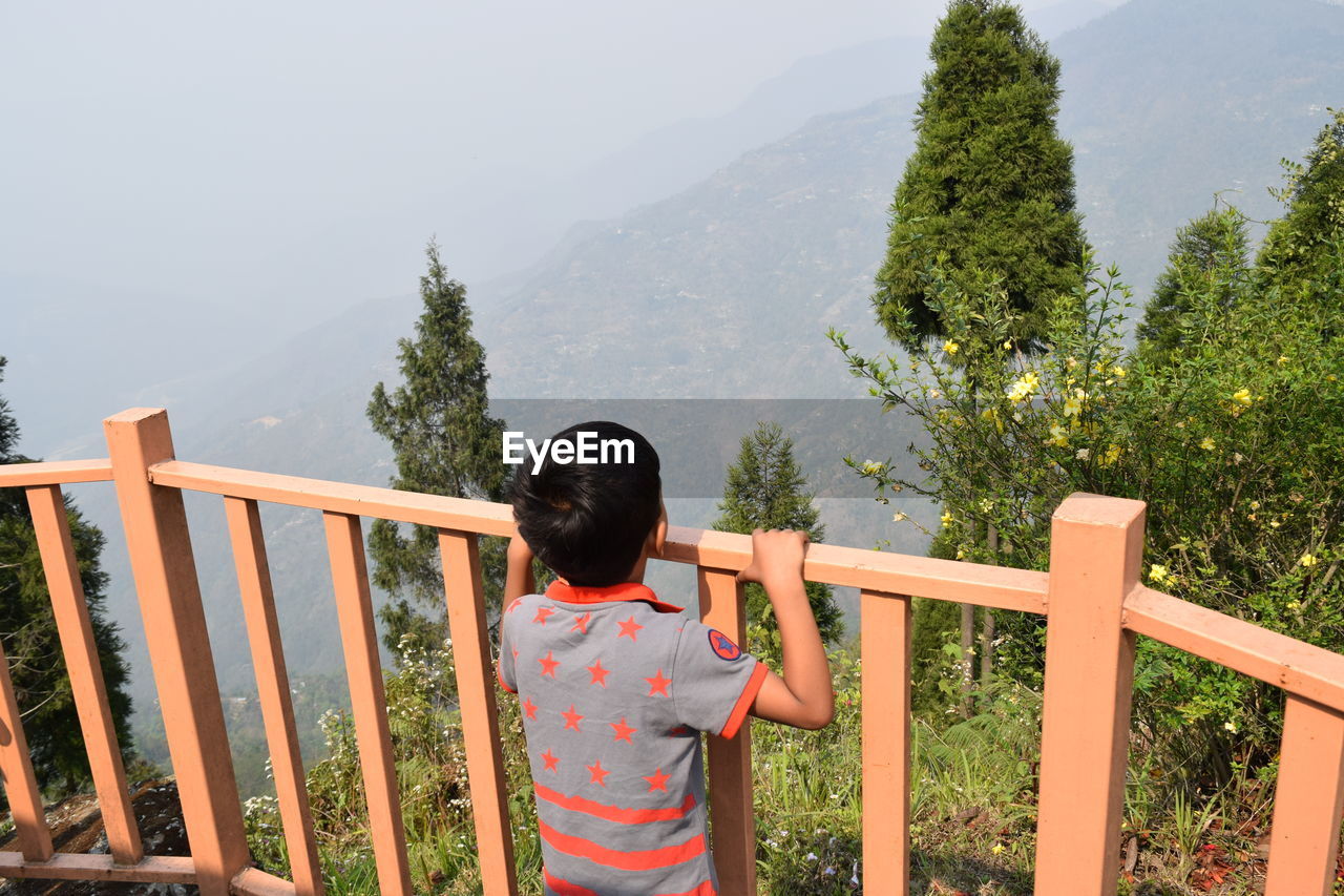 Rear view of boy standing by railing during foggy weather