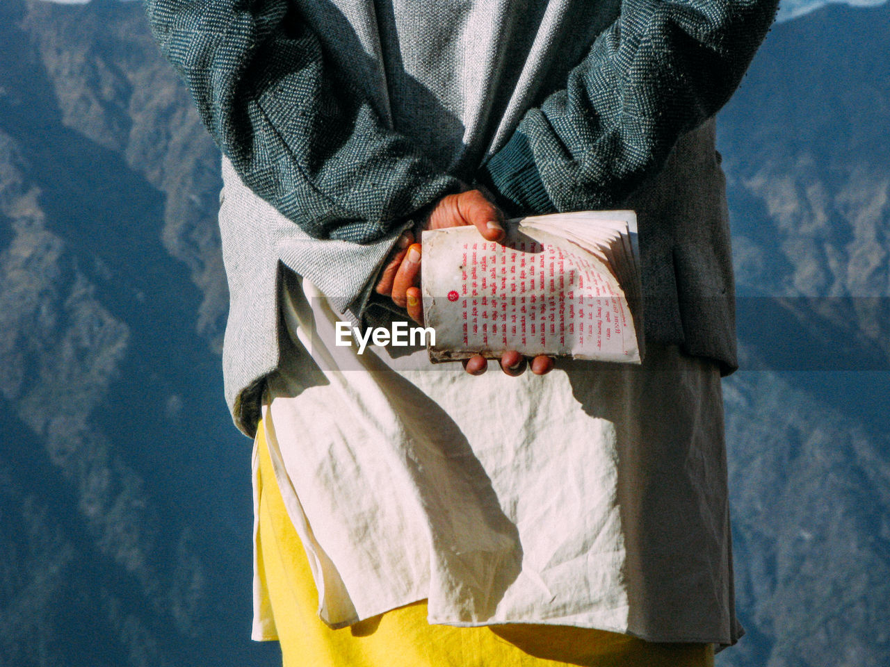 Midsection of woman holding book while standing against mountain