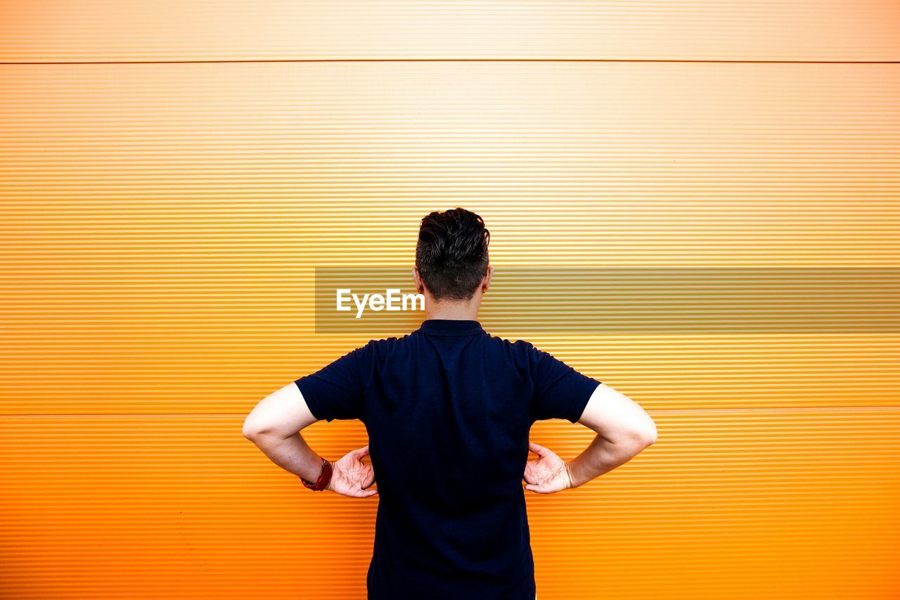 Rear view of man standing against orange wall