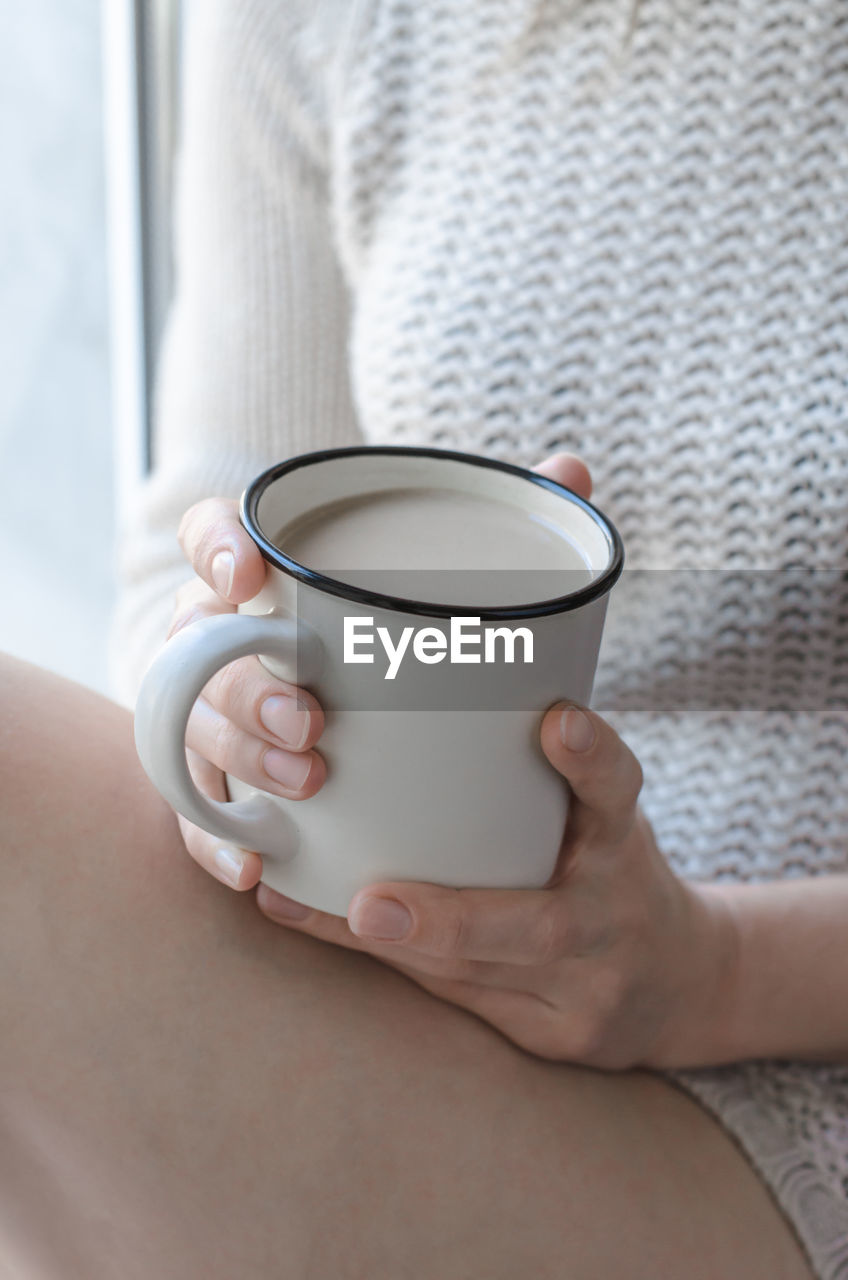 Cup of coffee in hands close-up. woman in knitted sweater holding a cup of coffee