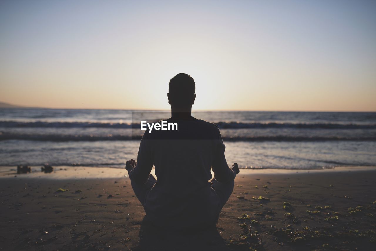 Young man in meditation near the sea. concept of pray. adult practice yoga on the beach at sunset.