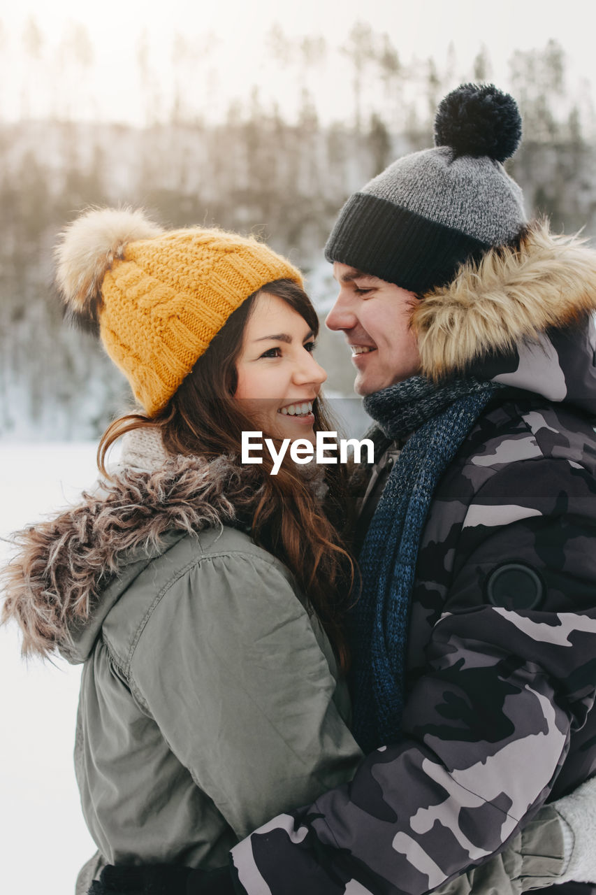 Happy couple in warm clothing embracing while standing outdoors