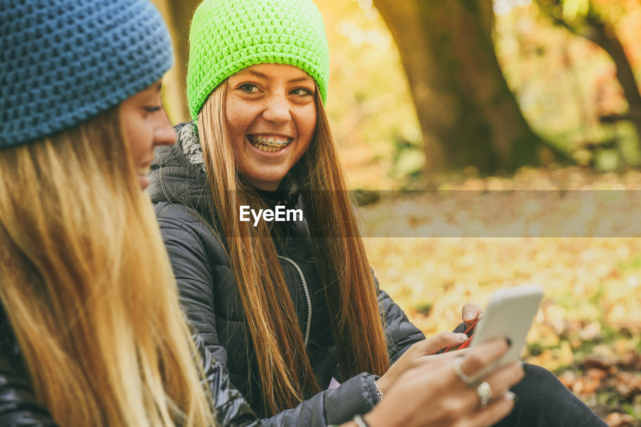 Girls with wool cap sitting in the park using smartphone. teen using mobile phone chat with friends